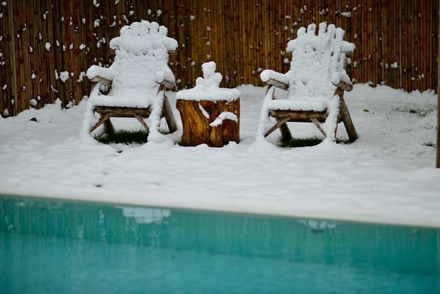 two lawn chairs sitting next to a pool covered in snow.