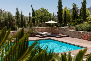 a pool surrounded by a stone wall and a wooden deck.